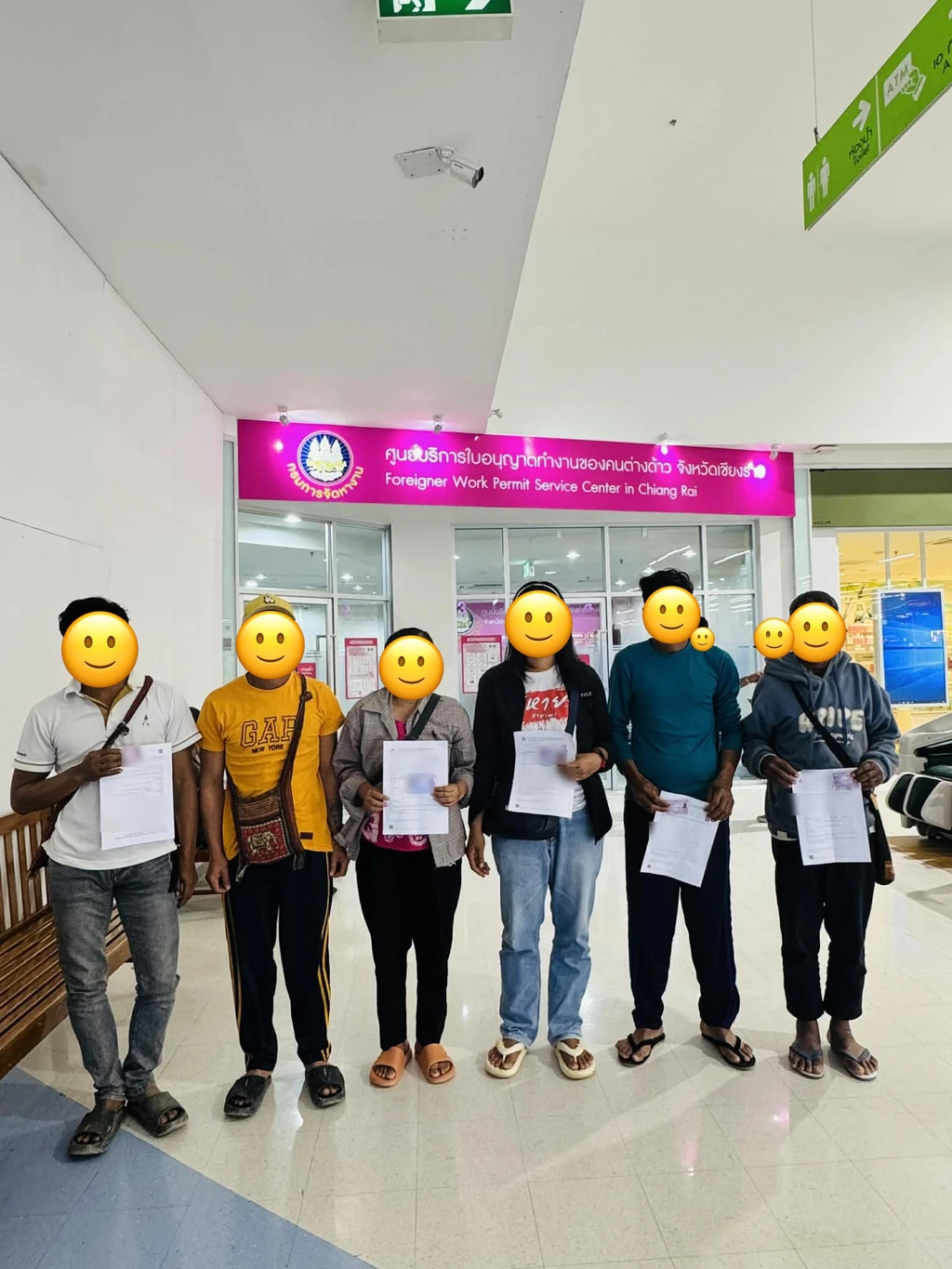 กลุ่มลูกจ้างต่างด้าวถือเอกสารคำขอใบอนุญาตทำงานขนาด A4 หลังยื่นเรื่องเสร็จ